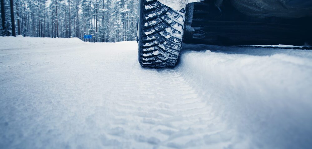 Car tire leaving tracks on snowy road.