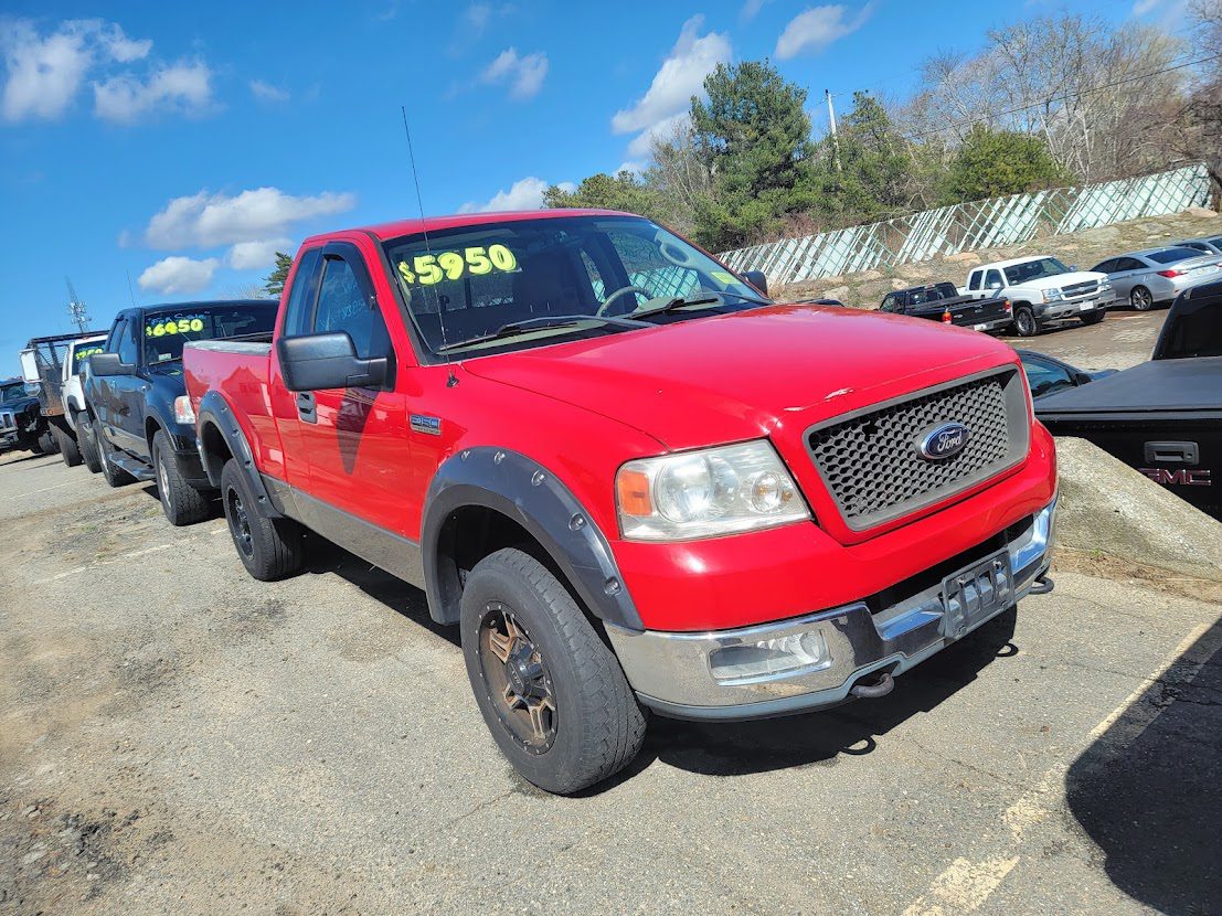 Red Ford pickup truck parked outdoors with a price displayed on the windshield.