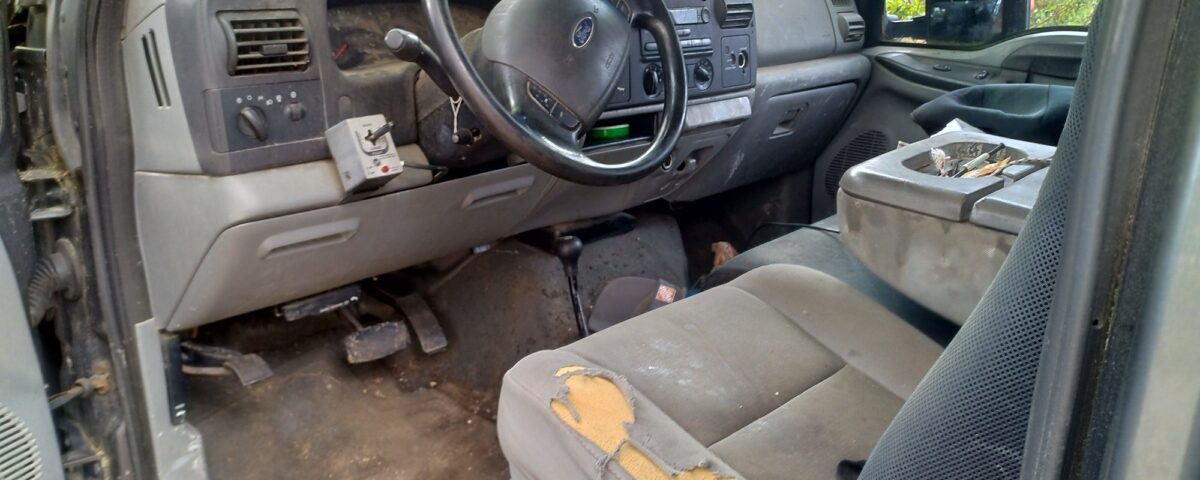 Worn-out car interior with torn seat cushions and dirty floor.