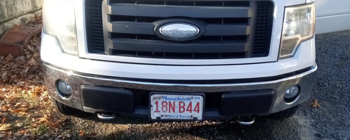 White Ford truck parked on a gravel driveway with the driver's door open.