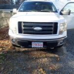 White Ford truck parked on a gravel driveway with the driver's door open.