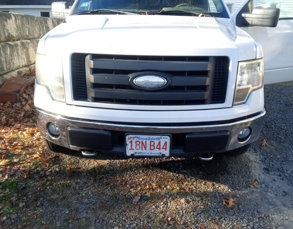White Ford truck parked on a gravel driveway with the driver's door open.
